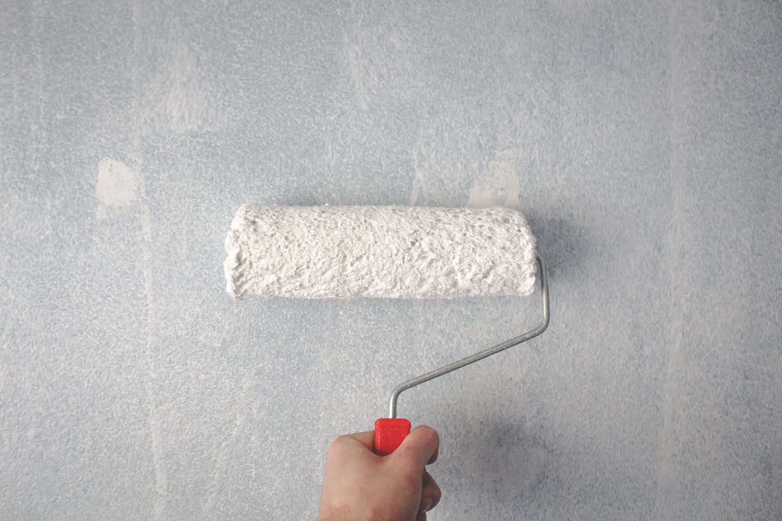Hand mit Farbrolle trägt weiße Farbe auf eine Wand auf